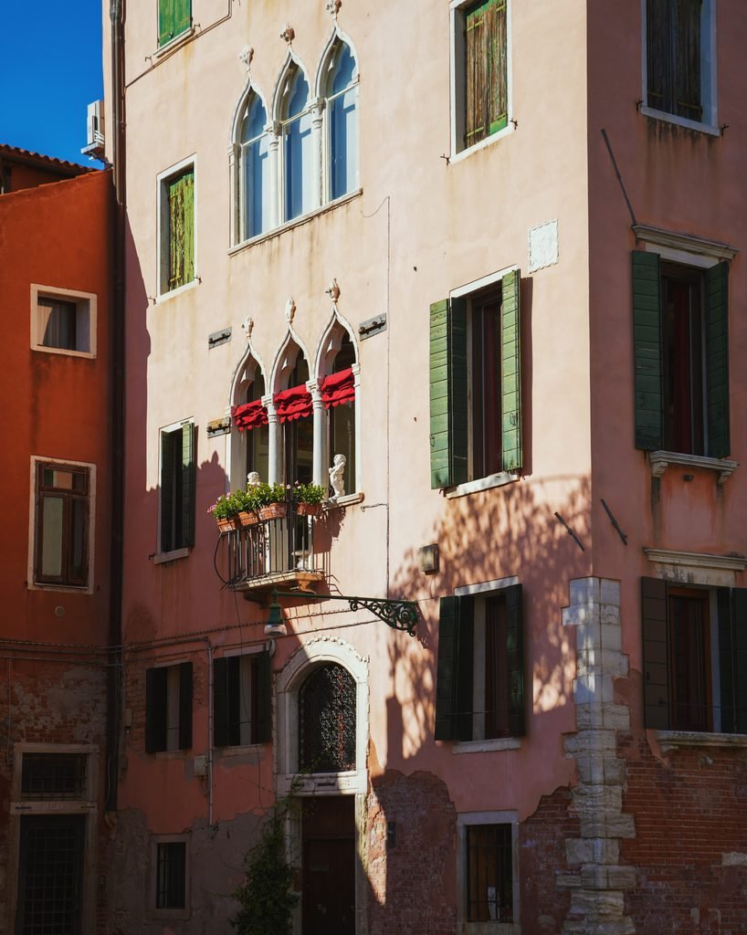Pastel Venetian palazzo with Gothic arched windows and green shutters in Venice