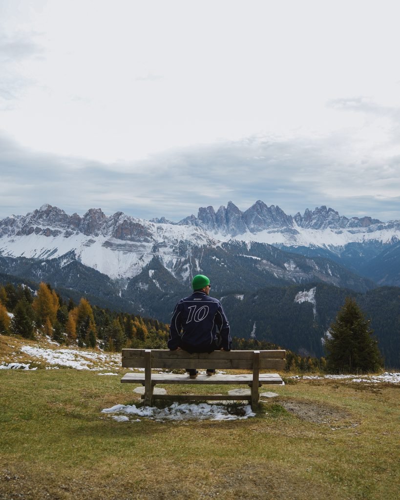 Daniel sitting on a bench on the Plose above Brixen, looking out at the snowy Odle peaks in the Dolomites