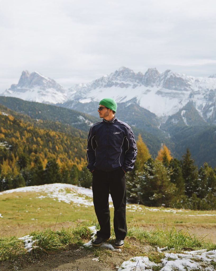 Daniel standing on the Plose in autumn with snow capped Dolomites peaks behind him